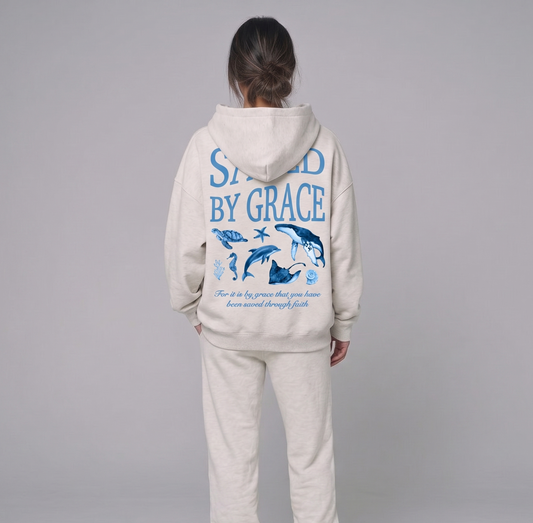 Person wearing a beige hoodie and pants set with 'Saved by Grace' text on the back, on a gray background.